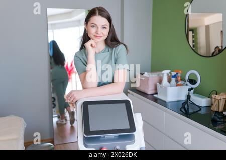 woman is standing in front machine with a white screen. She is smiling and she is happy, laser hair removal room Stock Photo