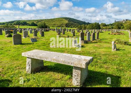 Corfe Castle, UK - September 14th 2023: A stone seat in front of gravestones in the God’s Acre Cemetery surrounded by countryside. Stock Photo