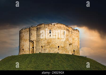 Dramatic sky over an ancient stone fortress atop a lush green hill, symbolizing historical strength and medieval architecture in York, North Yorkshire Stock Photo