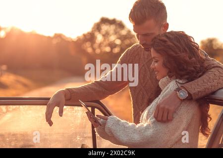 Beautiful couple on road trip, they are taking a break from driving and looking for direction on tablet. Stock Photo
