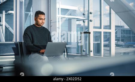 Airport Terminal: Indian IT Specialist, e-Commerce Businessman Uses Laptop Computer, Waiting for His Flight. Traveling Digital Entrepreneur Remote Work Online Sitting in Boarding Lounge of Airline Hub Stock Photo
