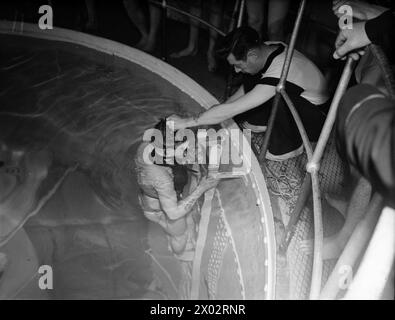 DAVIS APPARATUS BRINGS SUBMARINE-TRAPPED MEN TO SAFETY. 14 DECEMBER 1942, HMS DOLPHIN, AT GOSPORT, THE WAY TO SAFETY FOR BRITAIN'S UNDERWATER FIGHTERS SHOULD THEY BE TRAPPED IN A DOOMED SUBMARINE LIES THROUGH THE ESCAPE HATCH AND DAVIS SUBMERGED ESCAPE APPARATUS. WITH A RUBBER BAG FILLED FROM A SMALL CYLINDER OF COMPRESSED OXYGEN STRAPPED TO HIS CHEST, NOSTRILS CLOSED BY RUBBER CLIPS, EYES PROTECTED BY SPECIAL GOGGLES, THE SUBMARINE SAILOR CAN RISE SLOWLY TO THE SURFACE. HE BREATHES OUT THROUGH A CONTAINER OF CHEMICAL ABSORBENT WHICH PURIFIES THE AIR SO THAT IT CAN BE RE-INHALED. TRAINEES FOR Stock Photo