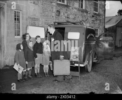 FILM SHOW AT HIGHEST VILLAGE IN THE HIGHLANDS: MINISTRY OF INFORMATION FILM SCREENING, TOMINTOUL, BANFFSHIRE, SCOTLAND, UK, 1943 - A group of local children look on as Ministry of Information Film Operator John Macdougall arrives outside the Memorial Hall in Tomintoul to set up his film equipment. He is unloading his van as he prepares to transform the village hall into a cinema for the evening. The film is due to start at 8pm Stock Photo