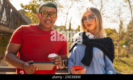 A young smiling multiracial couple holding smart phone and digital tablet,looking at camera Stock Photo