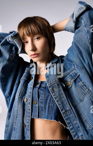 A stylish young woman with short hair striking a confident pose while wearing a jean jacket in a studio setting. Stock Photo