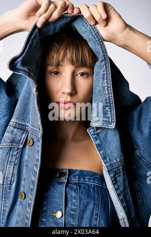 A young woman with short hair joyfully raises her jean jacket over her head in a studio setting. Stock Photo