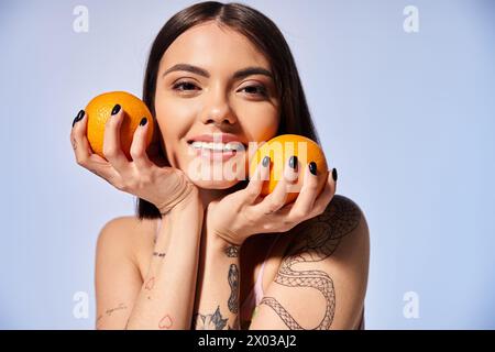 A young woman with brunette hair playfully holding two oranges in front of her face in a studio setting. Stock Photo