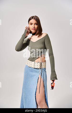 A young brunette woman gracefully dons a stylish skirt and cozy sweater in a studio setting. Stock Photo