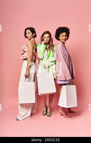 Three women of different ethnicities holding shopping bags on a pink background. Stock Photo