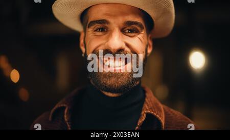 Portrait of a Handsome Man in Stylish Clothes and a Fedora Hat Posing for Camera. Happy Attractive Caucasian Multiethnic Gentleman Smiles on Warm Outdoors Background. Stock Photo