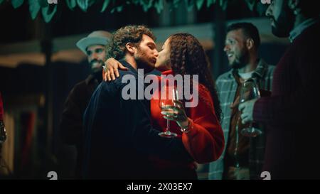 Loving Mixed Race Couple Dancing and Moving to Music at an Outdoors Terrace or Garden Party with Friends. Beautiful Man and Woman Kiss, Relax on Weekend, Have Fun and Drink Wine. Stock Photo