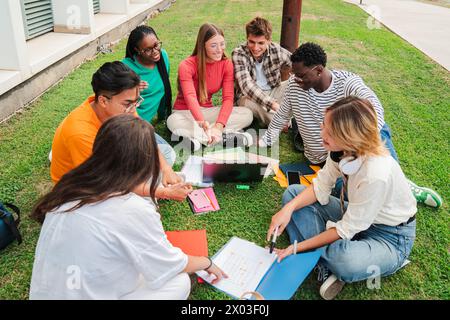 Multiracial students using a laptop computert sitting in a circle on the grass, doing homework outside at university campus. Young high school people working together on a academy task or schoolwork. High quality photo Stock Photo