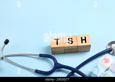 Endocrinology. Stethoscope, pills and wooden cubes with thyroid hormones on light blue background. Space for text Stock Photo