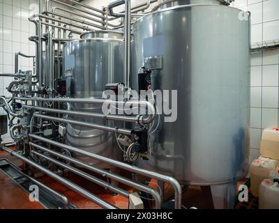 Modern brewery setup with large stainless steel fermentation tanks connected by sophisticated network of pipes. Brewing process, precise temperature control and sterilization. Stock Photo