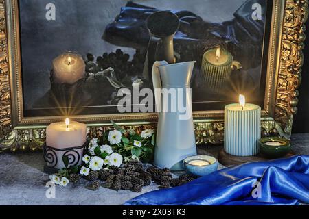 A still life with a blue satin fabric next to several lit candles, flowers and their reflection on a black surface Stock Photo