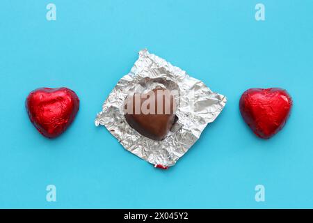 Two chocolates and one with an unwrapped wrapper.Three chocolate hearts on a blue background, top view. Stock Photo