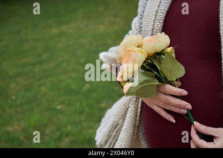 Pregnant woman's belly with a bouquet of flowers in her hand. She has a natural woollen blanket in white with grey. Stock Photo