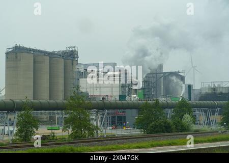 A factory releasing billowing smoke from its tall stacks into the sky, indicating active industrial processes and pollution. Stock Photo