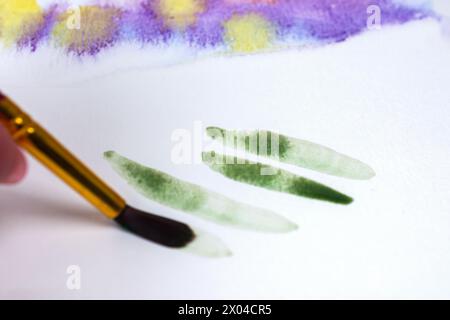 Artist practices basic wet on dry technique: wet paint on dry paper. Stock Photo