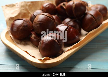 Fresh edible sweet chestnuts in serving plate on light blue wooden table, closeup Stock Photo