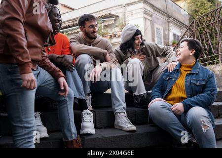Group of multicultural friends sharing laughter and joy sitting on city steps - Young adults showcasing the spirit of urban youth and diverse friendsh Stock Photo