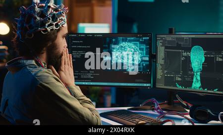 IT technician using EEG headset stupefied after mind upload virtual process is successful. Man astounded after achieving goal of transferring consciousness into computer cyberspace, camera A Stock Photo