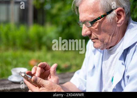 Reflective elderly male browsing his smartphone, merging the serenity of a green park with the digital ages pulse. High quality photo Stock Photo