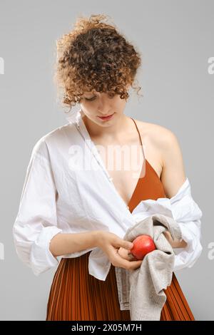 Woman wiping an apple with a towel over grey background. Concept of healthy eating and vitamins in ordinary products Stock Photo
