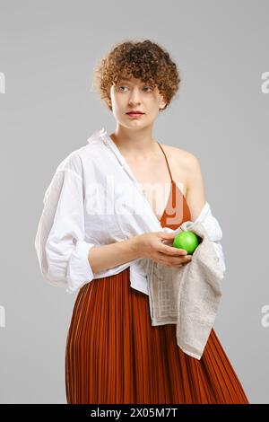 Woman wiping an apple with a towel and looking to the side. Concept of healthy eating and vitamins in ordinary products Stock Photo