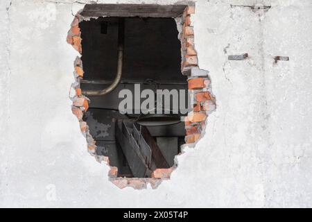 Large hole in an old brick wall. There's a lantern hanging behind the wall Stock Photo