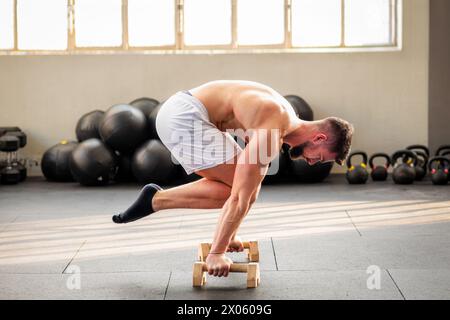 Side view of strong muscular male doing Tuck planche calisthenics exercise on floor in gym with Wooden parallettes Stock Photo
