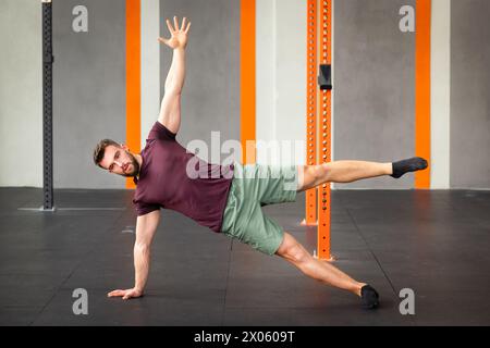 Side view of fit male performing calisthenics star side plank exercise on floor in modern gym Stock Photo