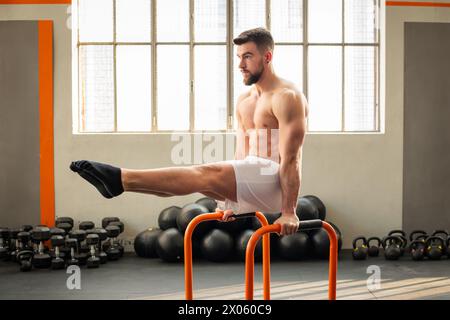 Side view of muscular male doing L sit on parallel bars calisthenics exercise in modern fitness club Stock Photo