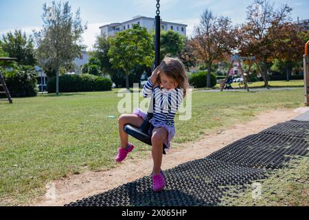 A little cute girl walks on the playground on a sunny summer day. The girl rides on a slide, a bungee, and climbs a slide. Stock Photo