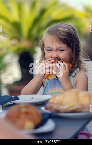 A beautiful little girl eats a croissant with chocolate with appetite. The girl has breakfast with a croissant. Caucasian girl eats pastries. Close-up Stock Photo