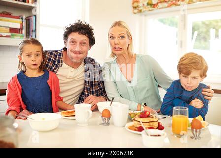 Family, portrait and funny face with children in kitchen for silly, comic and bonding together. Food, happy mother and father with young kids for Stock Photo