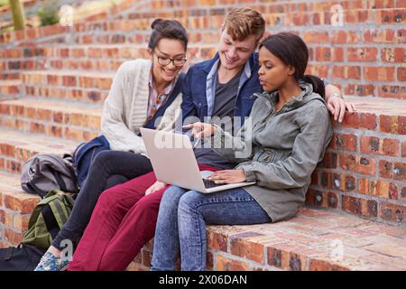 Happy, group of students and laptop, sitting or bonding with laptop outside on campus stairs. College people, smile and computer with teamwork and Stock Photo