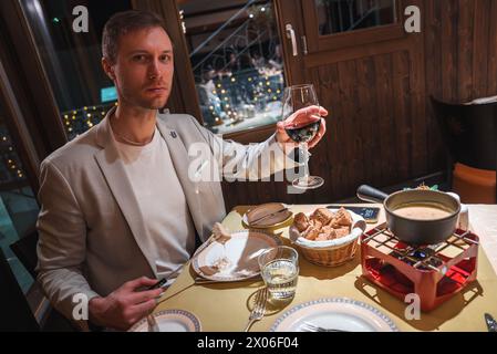 Man in Beige Blazer Enjoying Fondue Dinner at Cozy Alpine Restaurant Stock Photo
