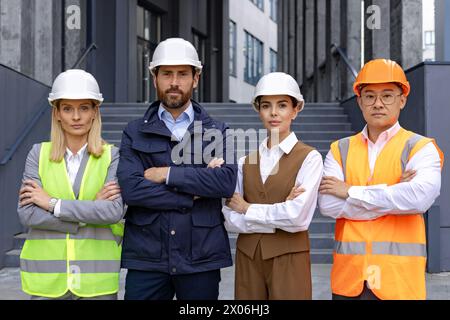 Portrait of an interracial group of men and women, a team of engineers and construction workers standing outside an office, crossing their arms over their chests and looking into the camera. Stock Photo