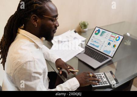 Businesswoman using a calculator to calculate numbers on a company's financial documents, she is analyzing historical financial data to plan how to Stock Photo
