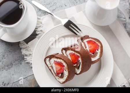 Chocolate cake roll with fresh strawberries and cream cheese closeup on a marble background. Horizontal top view from above Stock Photo