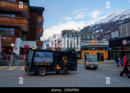 Bustling street scene in Zermatt, Switzerland, with electric taxis, alpine architecture, and shops. Stock Photo