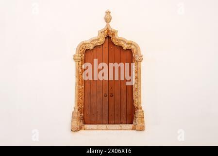 Ornate plaster window frame with closed wooden shutters in a white wall. Stock Photo