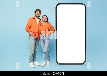 Couple standing with a giant smartphone on blue background Stock Photo