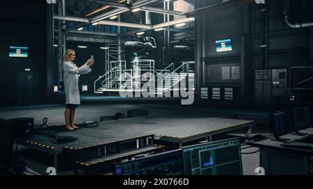 Female Engineer Uses Tablet Computer while Working in an Industial Facility at a Factory. Scientist uses Augmented Reality Software. Empty Space Left for Mock Up Template for VFX. Stock Photo