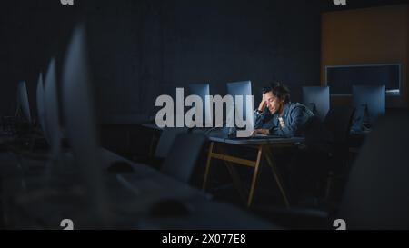 Stressed Male Student Sitting Alone in College Informatics Room, Working Late Evenings on Computer Science Project. Tired Scholar Study IT on Computer in University, Writing Homework. Stock Photo