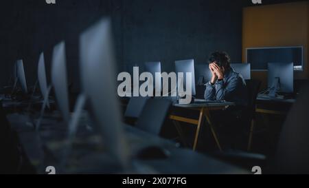 Stressed Male Student Sitting Alone in College Informatics Room, Working Late Evenings on Computer Science Project. Tired Scholar Study IT on Computer in University, Writing Homework. Stock Photo