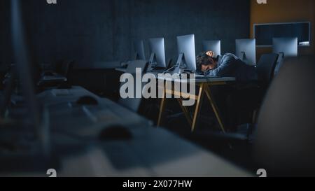 Stressed Male Student Sitting Alone in College Informatics Room, Working Late Evenings on Computer Science Project. Tired Scholar Study IT on Computer in University, Writing Homework. Stock Photo