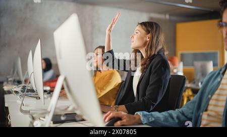 Beautiful Smart Female Student, Studying in University with Diverse Multiethnic Classmates. She Raises Hand and Asks Teacher a Question. Applying Her Knowledge to Acquire Academic Skills in Class. Stock Photo