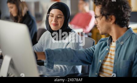 Female Muslim Student Wearing Hijab, Studying in Modern University with Diverse Multiethnic Classmates. She Asks Scholar a Question in College Room. Learning Software Engineering or Computer Science. Stock Photo